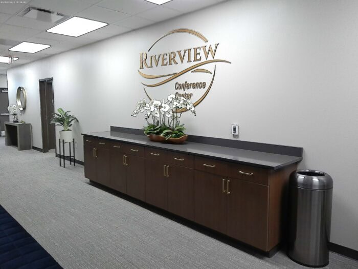 Hallway with brown cabinets, white orchids, a trash can, and a wall sign reading "Riverview Conference Center" reflects top-notch facility maintenance.