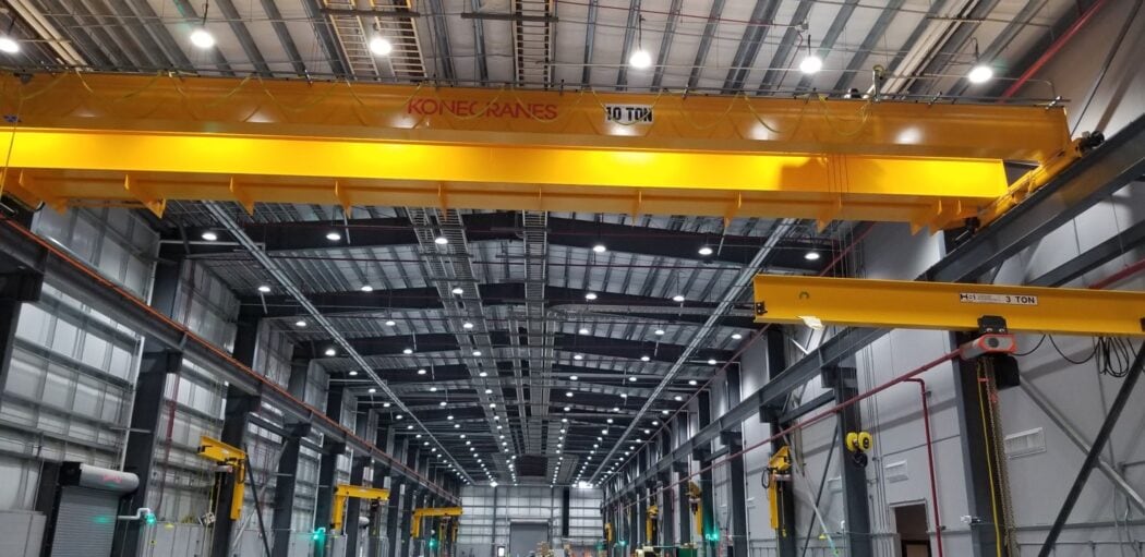 Industrial warehouse buildings under construction with multiple yellow overhead cranes and a red mobile platform. The floor is unfinished.