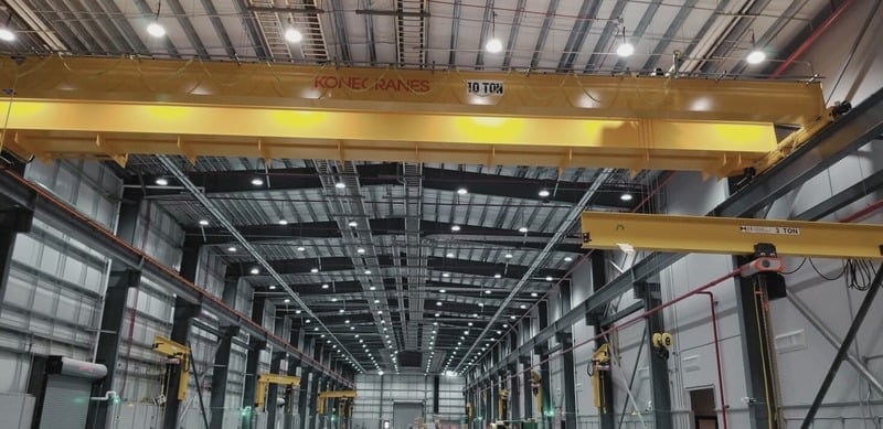 Interior of a large industrial warehouse with high ceilings, multiple overhead cranes, and exposed beams in a shop for maintenance buildings.